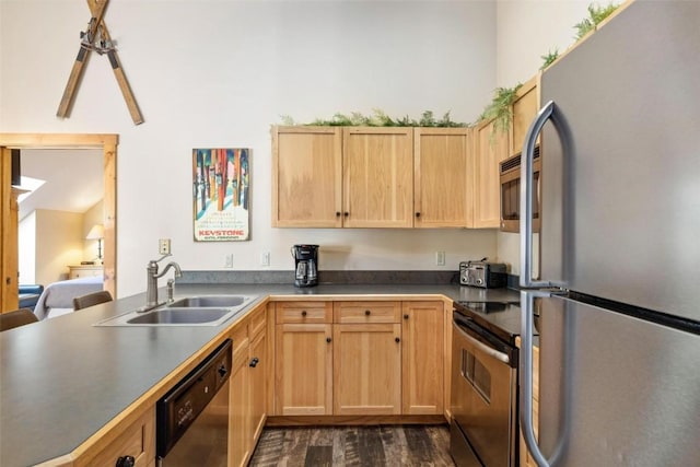kitchen with light brown cabinets, a sink, stainless steel appliances, a peninsula, and dark wood-type flooring