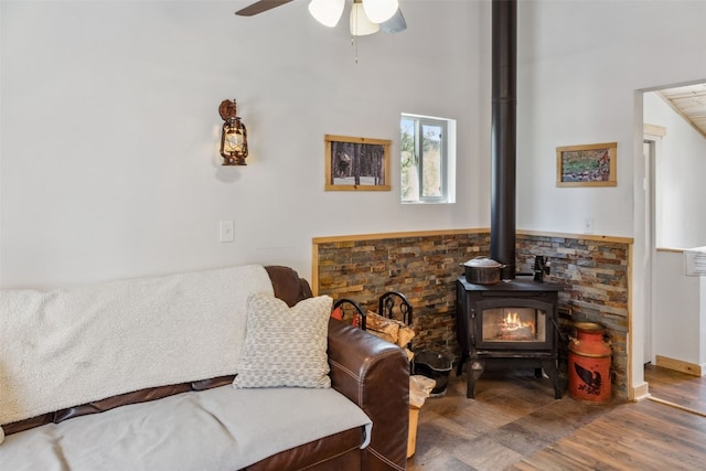 living area with a wood stove, a ceiling fan, and wood finished floors
