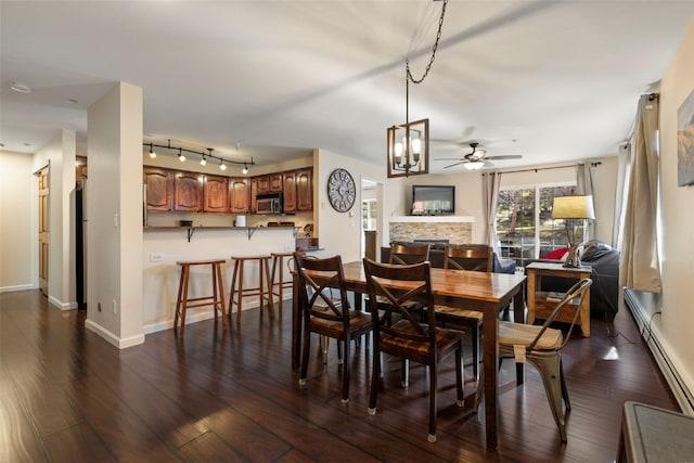 dining room featuring a ceiling fan, dark wood-style floors, a stone fireplace, and baseboards