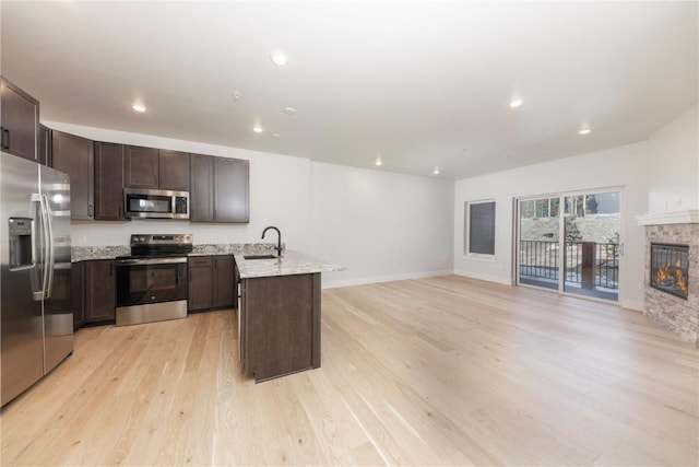 35 Argentine Ct Unit 204, Keystone, CO 80435 - kitchen featuring appliances with stainless steel finishes, a peninsula, dark brown cabinetry, light wood finished floors, and a glass covered fireplace