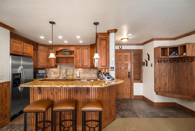 kitchen featuring a breakfast bar, light stone counters, crown molding, stainless steel fridge with ice dispenser, and kitchen peninsula