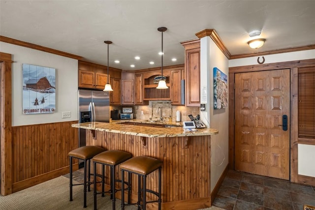 kitchen featuring crown molding, hanging light fixtures, stainless steel refrigerator with ice dispenser, light stone counters, and kitchen peninsula