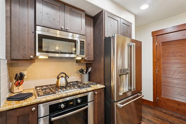 1521 Ski Hill Rd Unit 8312, Breckenridge, CO 80424 - kitchen with appliances with stainless steel finishes, dark wood-style floors, decorative backsplash, dark brown cabinetry, and light stone countertops