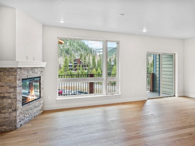 unfurnished living room with healthy amount of natural light, light wood finished floors, a glass covered fireplace, and recessed lighting