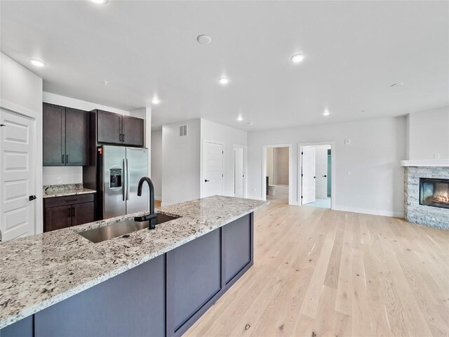 kitchen with stainless steel fridge, a sink, light wood-type flooring, open floor plan, and light stone countertops
