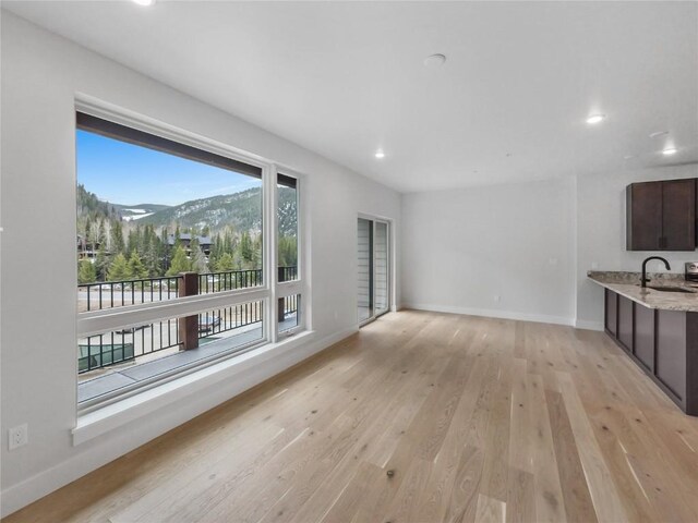 unfurnished living room with light wood-style flooring, a mountain view, baseboards, recessed lighting, and a sink