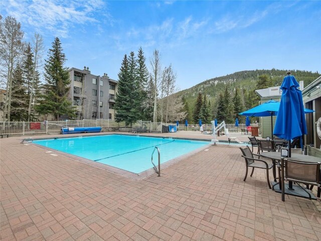 community pool with fence, a mountain view, and a patio area