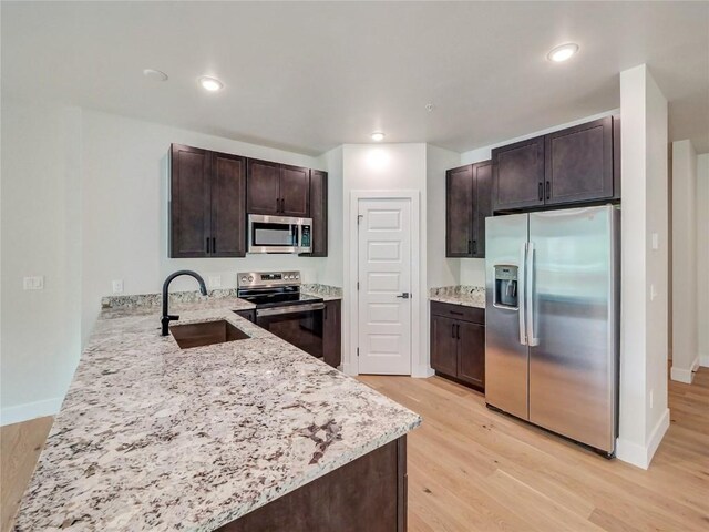 kitchen featuring appliances with stainless steel finishes, a sink, dark brown cabinetry, light wood finished floors, and recessed lighting