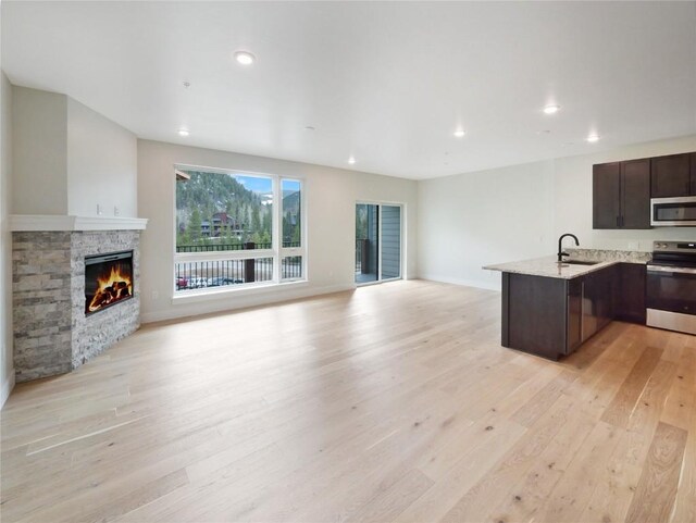kitchen with appliances with stainless steel finishes, open floor plan, a sink, dark brown cabinets, and light wood finished floors