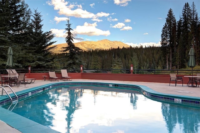 community pool featuring a forest view, fence, and a patio area