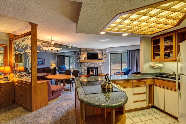 kitchen with a sink, cooktop, glass insert cabinets, a fireplace, and a peninsula