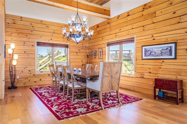 dining area featuring beamed ceiling, wooden walls, wood finished floors, and an inviting chandelier