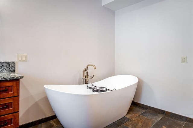 full bathroom with a freestanding bath, stone tile flooring, vanity, and baseboards