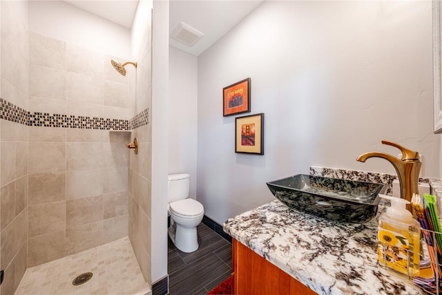 bathroom with toilet, tiled shower, visible vents, baseboards, and vanity