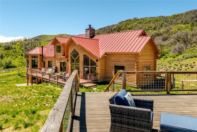 back of house featuring a chimney, a standing seam roof, a deck with mountain view, and metal roof