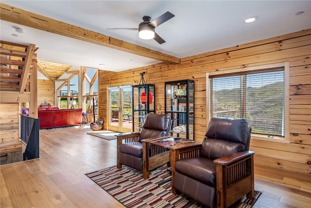 living room with beamed ceiling, wood finished floors, wood walls, and a ceiling fan