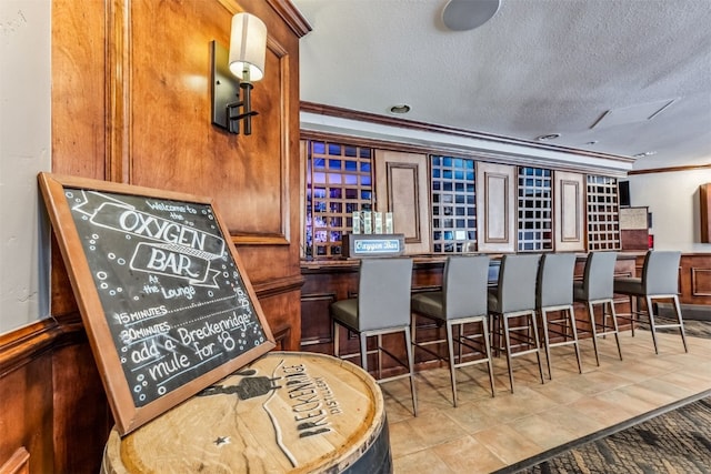 bar featuring ornamental molding, a textured ceiling, and light tile patterned floors