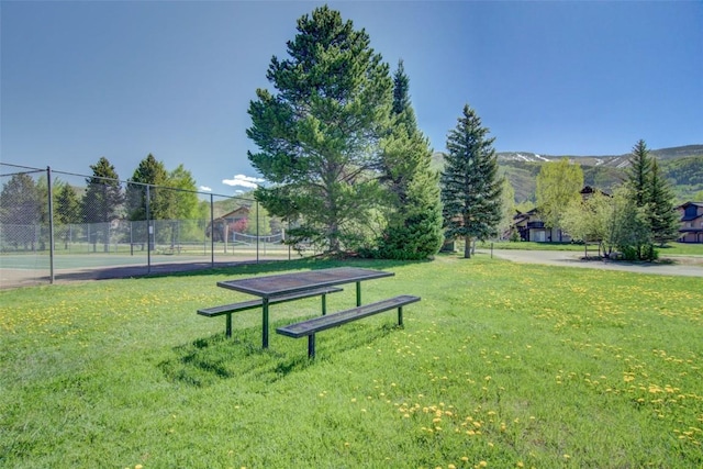 view of home's community featuring a yard, a tennis court, and fence