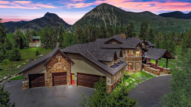 exterior space with a mountain view, driveway, stone siding, stucco siding, and a chimney