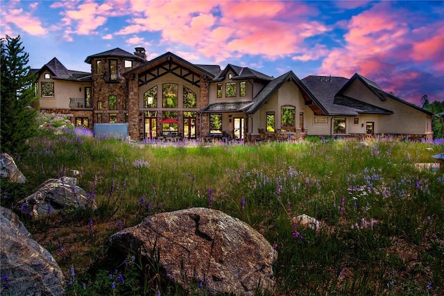 back of house featuring stone siding, a chimney, and stucco siding