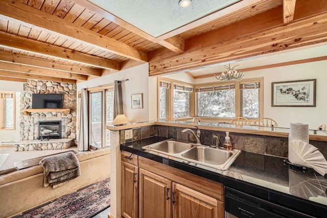 kitchen featuring dark countertops, dishwashing machine, a sink, a fireplace, and open floor plan