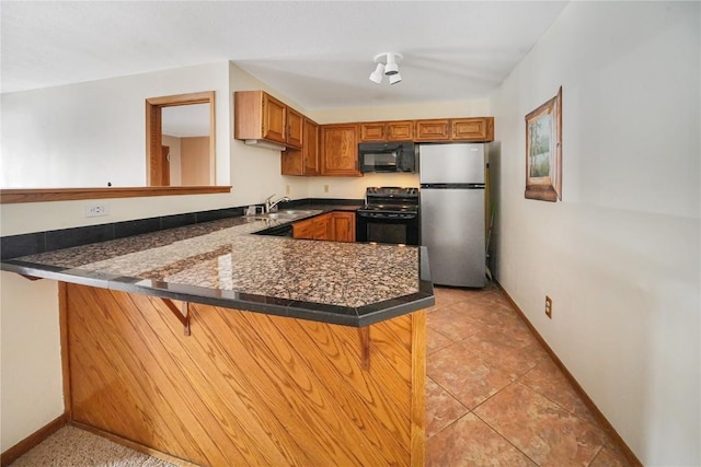 kitchen featuring a peninsula, dark countertops, brown cabinets, a sink, and black appliances