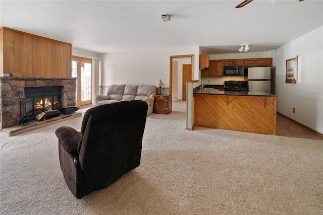 living area featuring a ceiling fan, a stone fireplace, and light colored carpet