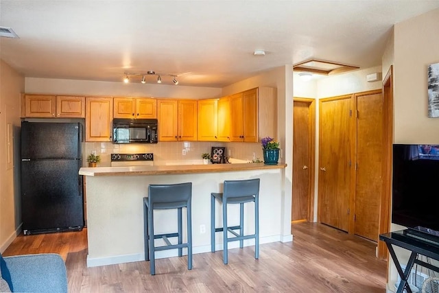 kitchen featuring backsplash, light wood-type flooring, light countertops, a peninsula, and black appliances