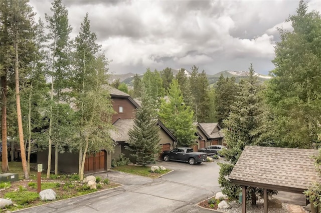 exterior space featuring a mountain view, driveway, an attached garage, and a shingled roof