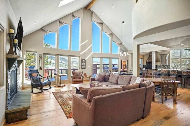 living room featuring french doors, lofted ceiling with beams, an inviting chandelier, light wood-style floors, and a glass covered fireplace