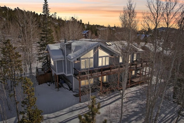 snow covered back of property with a wooden deck and a chimney