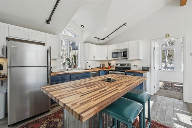 kitchen with blue cabinets, wood counters, vaulted ceiling, and appliances with stainless steel finishes