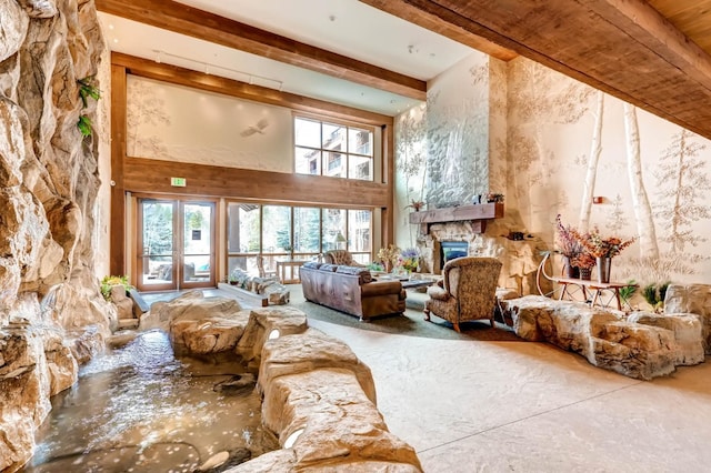 living area featuring beamed ceiling, a stone fireplace, and a towering ceiling