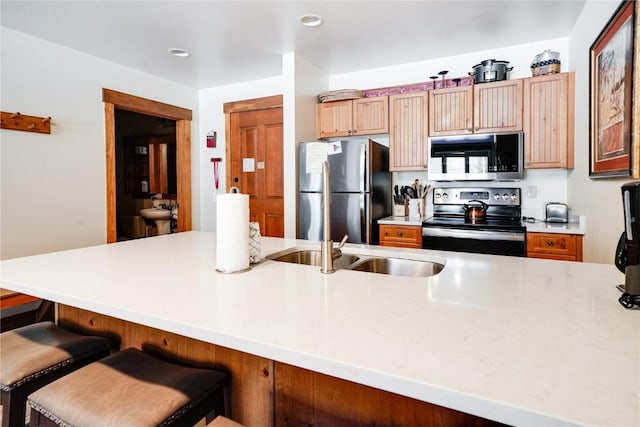 kitchen featuring a breakfast bar area, stainless steel appliances, a sink, and light countertops