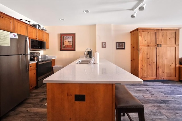 kitchen featuring stainless steel appliances, dark wood-style flooring, a sink, a kitchen breakfast bar, and light countertops