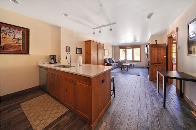 kitchen featuring dark wood-style floors, stainless steel dishwasher, brown cabinetry, a sink, and a peninsula