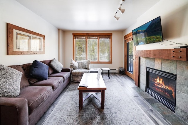 living room with a baseboard heating unit, a tile fireplace, track lighting, and wood finished floors