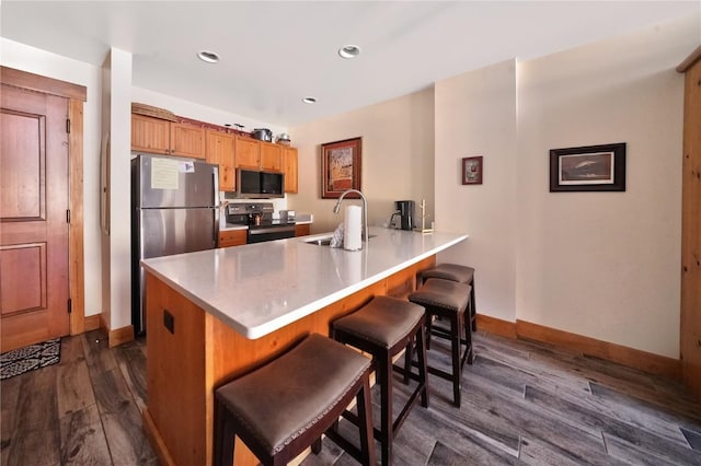 kitchen with a peninsula, a breakfast bar, a sink, appliances with stainless steel finishes, and dark wood finished floors