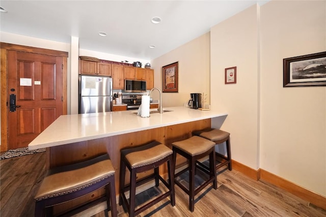 kitchen with a breakfast bar area, stainless steel appliances, a peninsula, wood finished floors, and a sink