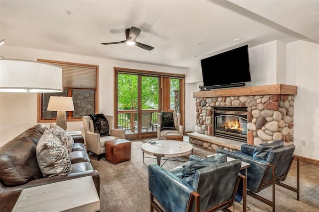 carpeted living room featuring a stone fireplace, a ceiling fan, and baseboards