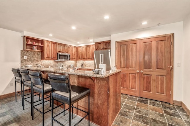 kitchen featuring stainless steel appliances, open shelves, baseboards, decorative backsplash, and a breakfast bar area