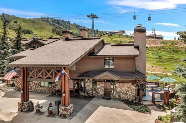 exterior space with a chimney, stone siding, and a shingled roof