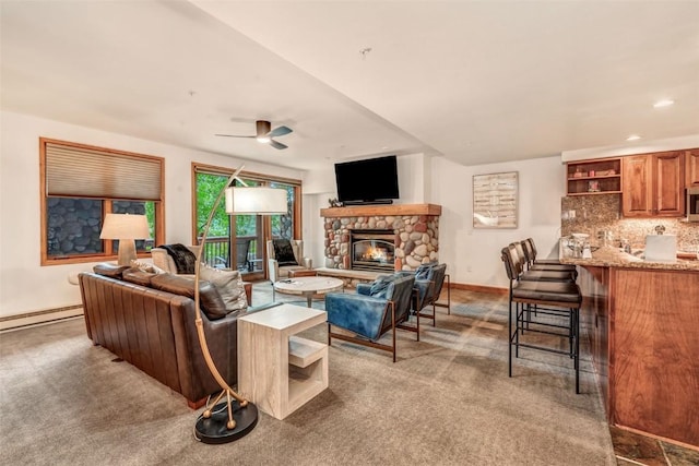 living room featuring baseboards, a ceiling fan, baseboard heating, a stone fireplace, and carpet floors