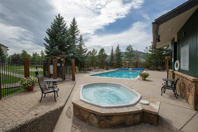 community pool with fence, a patio area, and a hot tub