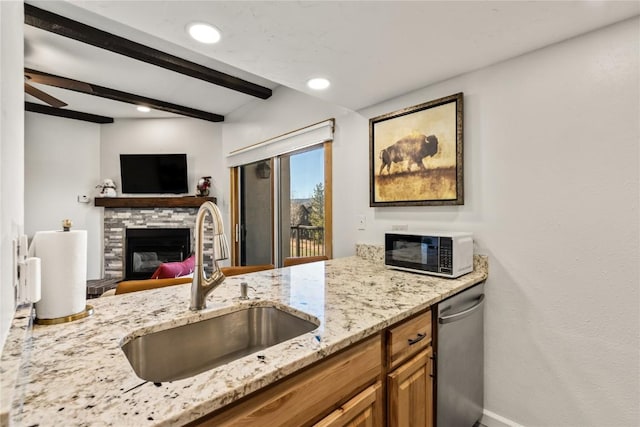 kitchen featuring dishwasher, a sink, light stone countertops, beam ceiling, and a fireplace