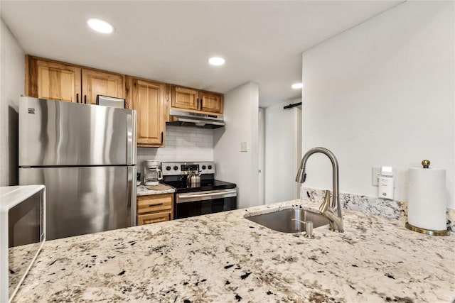 kitchen with under cabinet range hood, light stone counters, appliances with stainless steel finishes, and a sink