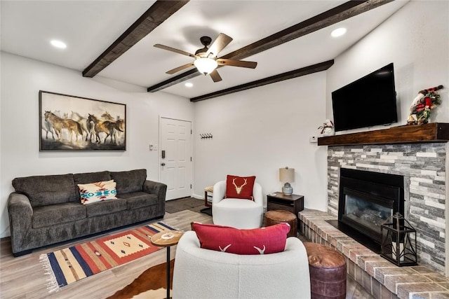 living area with a glass covered fireplace, a ceiling fan, wood finished floors, and beam ceiling