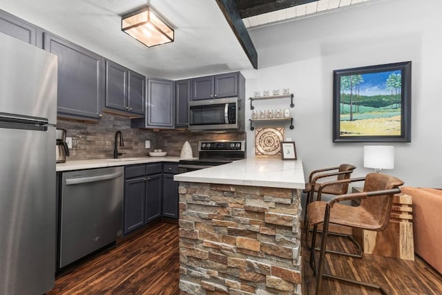 kitchen with a sink, appliances with stainless steel finishes, light countertops, a peninsula, and dark wood-style flooring