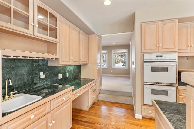 kitchen with light wood-style flooring, a sink, light brown cabinetry, double oven, and backsplash