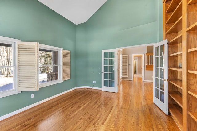 spare room with baseboards, high vaulted ceiling, wood finished floors, and french doors